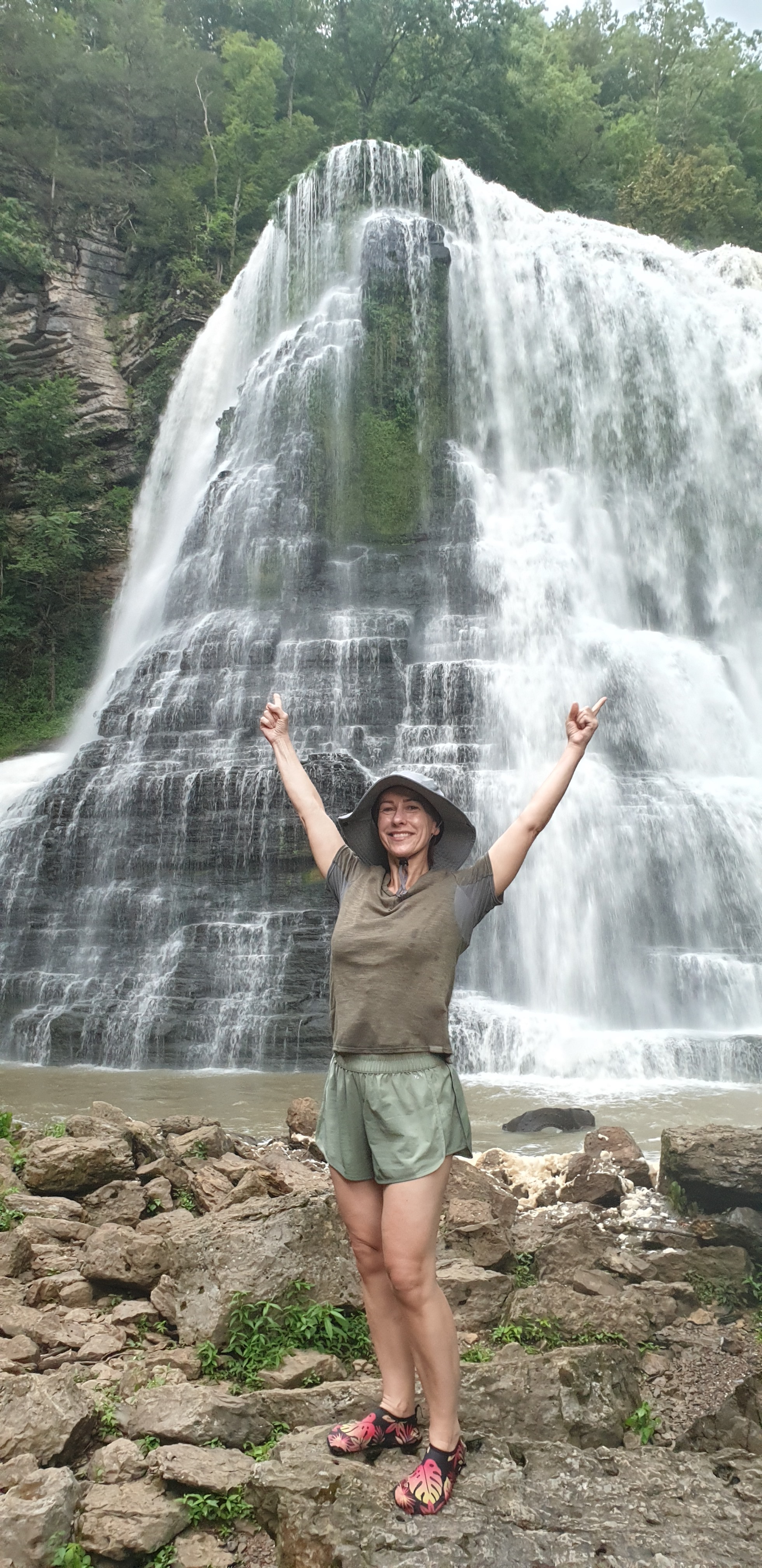 Joanna smiling with raised arms in front of a waterfall.